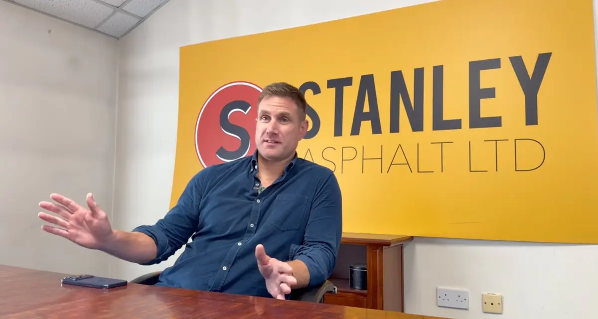 Neil Stanley at a table in front of the Stanley Asphalt sign.